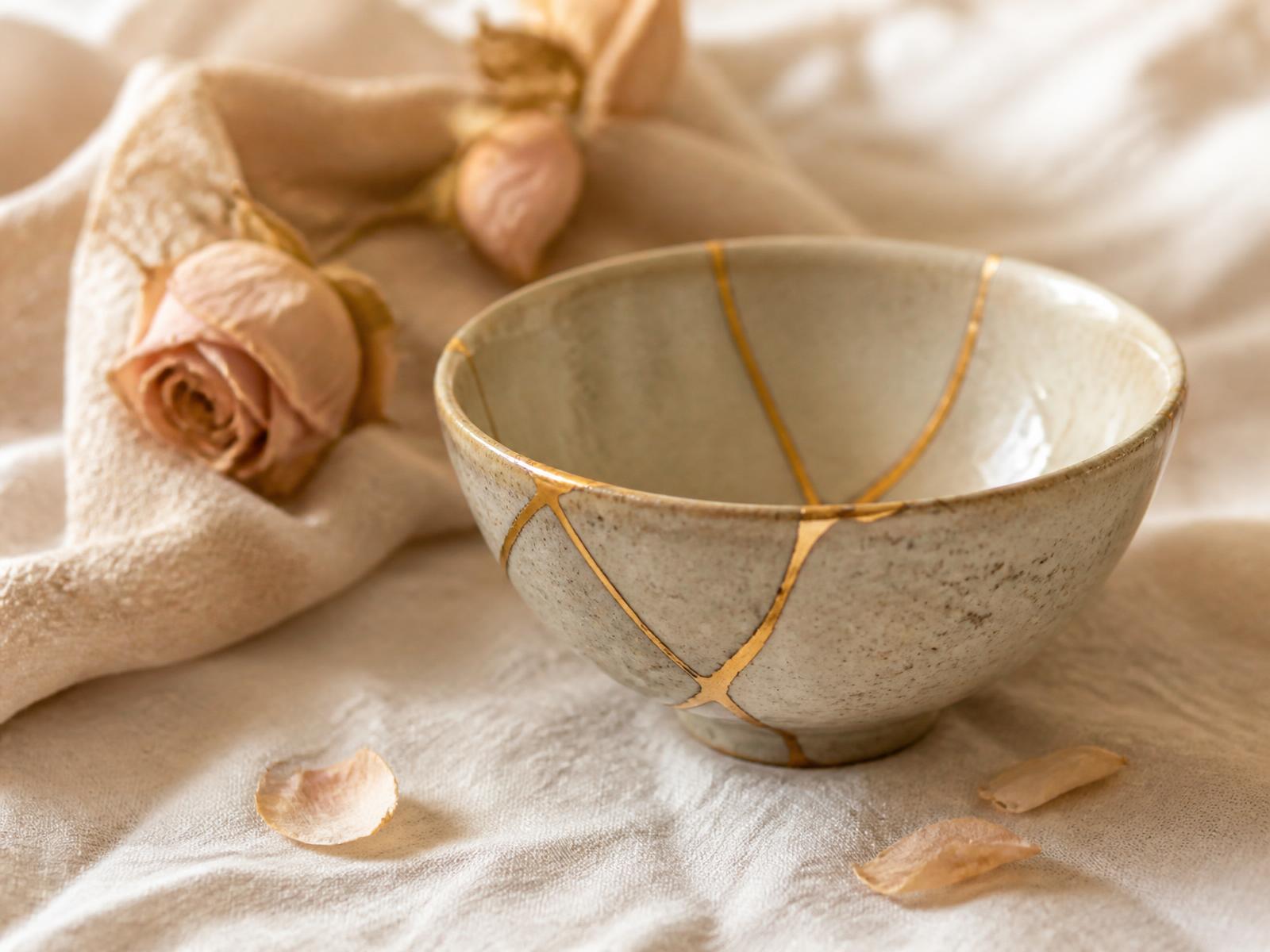 A ceramic bowl repaired with gold seams resting on ivory linen